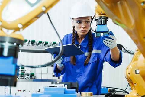 A female production line worker checks robotic equipment using a tablet computer.